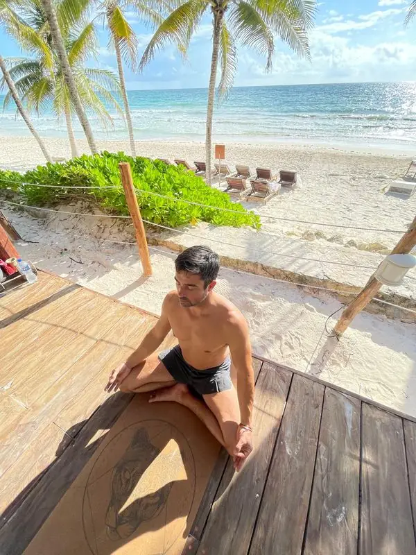 Travis meditating cross-legged on beach deck by ocean