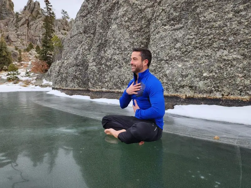 Travis meditating barefoot on frozen lake beneath granite cliff