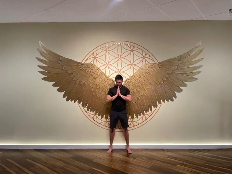 Prayer pose before golden angel wings yoga studio mural