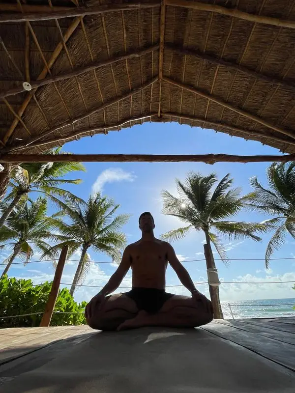Lotus meditation under beach palapa, sun through palms and ocean