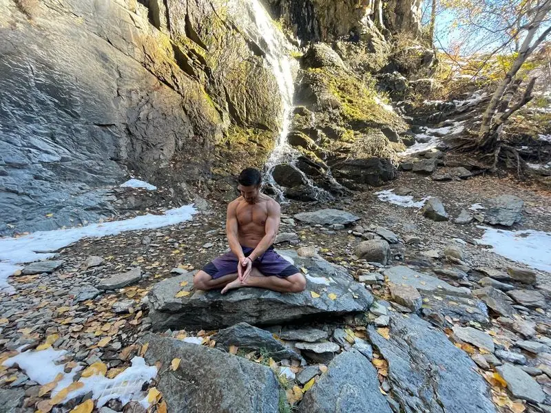 Meditating on rock before waterfall, autumn leaves
