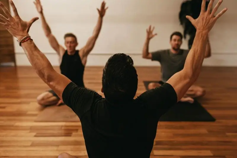 Travis leading small class, arms raised, wood-floor studio