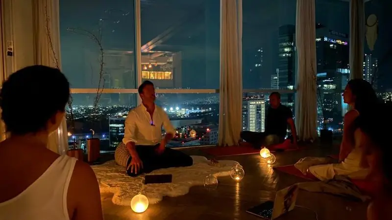 Travis leading candlelit nighttime breathwork with city skyline view