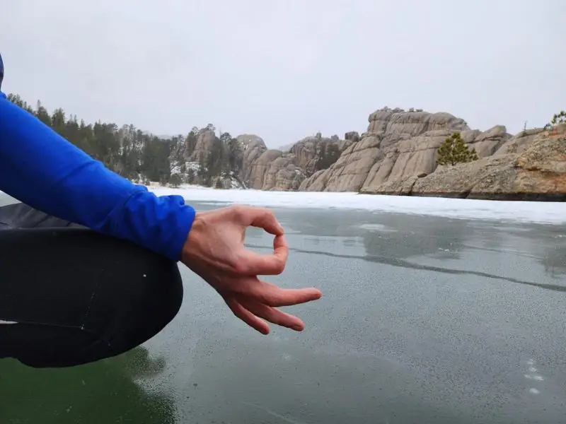 Mudra hand close-up over frozen lake, rock formations