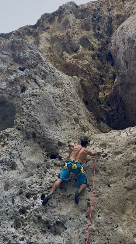 Shirtless climber ascending pocketed volcanic rock wall