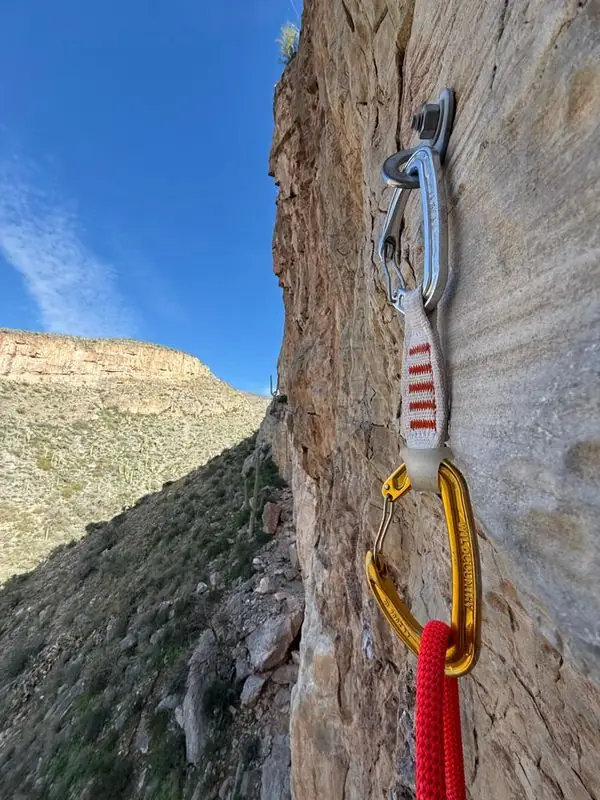 Quickdraws bolted on cliff face above desert canyon