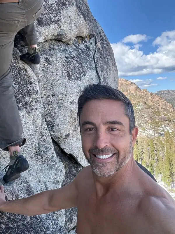Summit selfie with climber scaling granite boulder behind