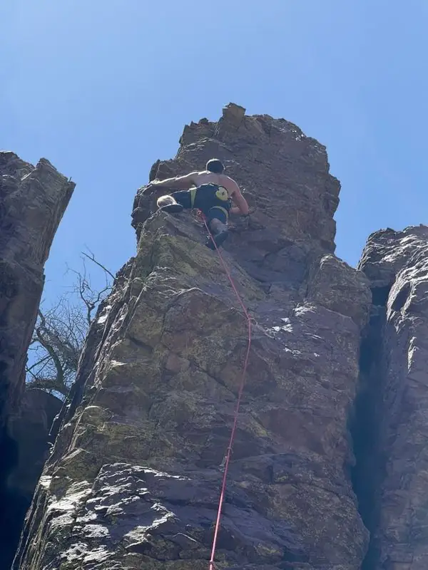 Shirtless climber topping out steep rock pinnacle on rope