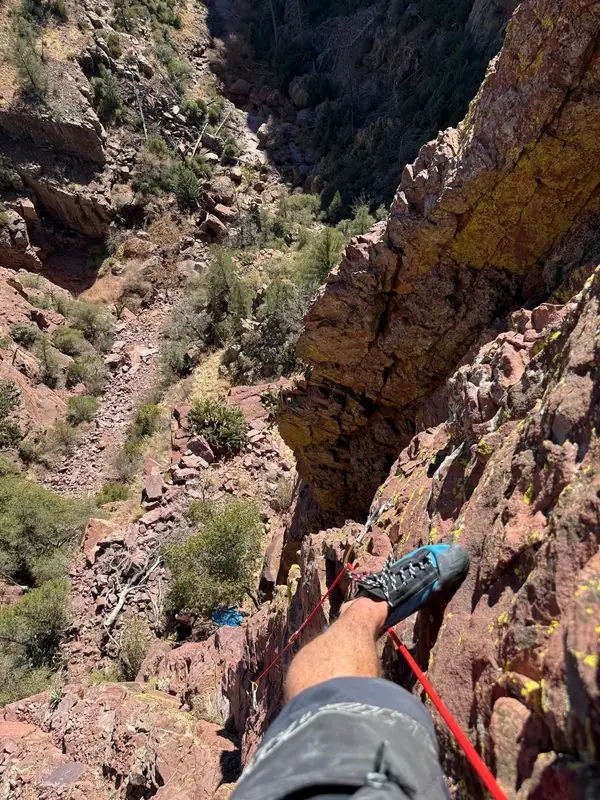 Climber's-eye view down cliff with rope and canyon below