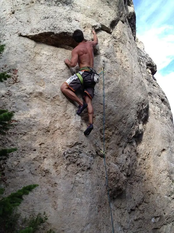 Shirtless sport climbing on steep limestone wall with rope
