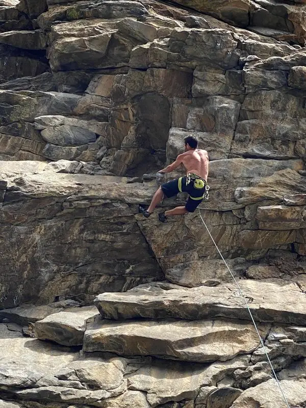 Shirtless lead climbing layered cliff with rope