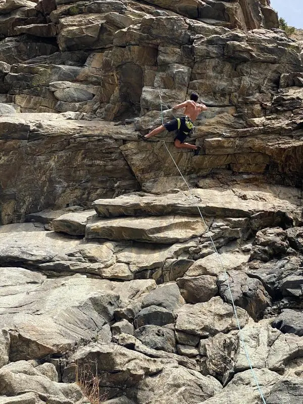 Shirtless climber mid-route on steep rock wall