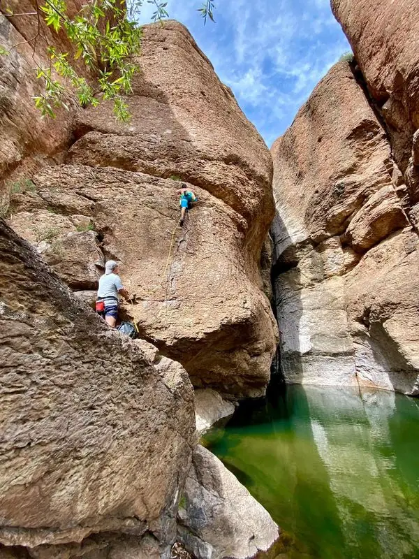 Climber on canyon wall above emerald pool, belayer below