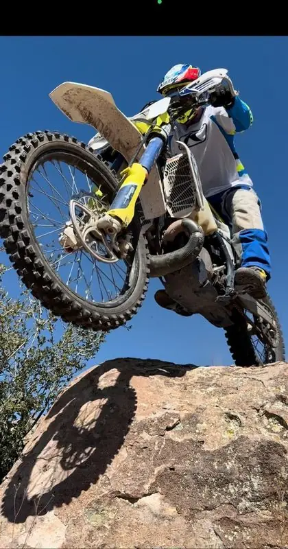 Wheelie up boulder on dirt bike, low angle