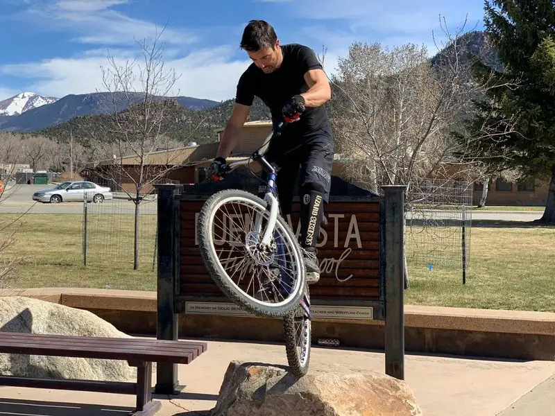 Trials bike balanced on boulder by school sign, mountains