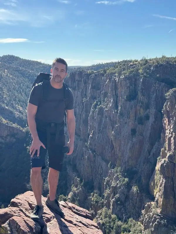 Travis with backpack posed on canyon rim, cliffs behind