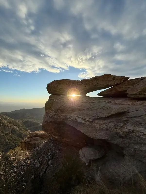 Sun flaring through rock arch above desert valley
