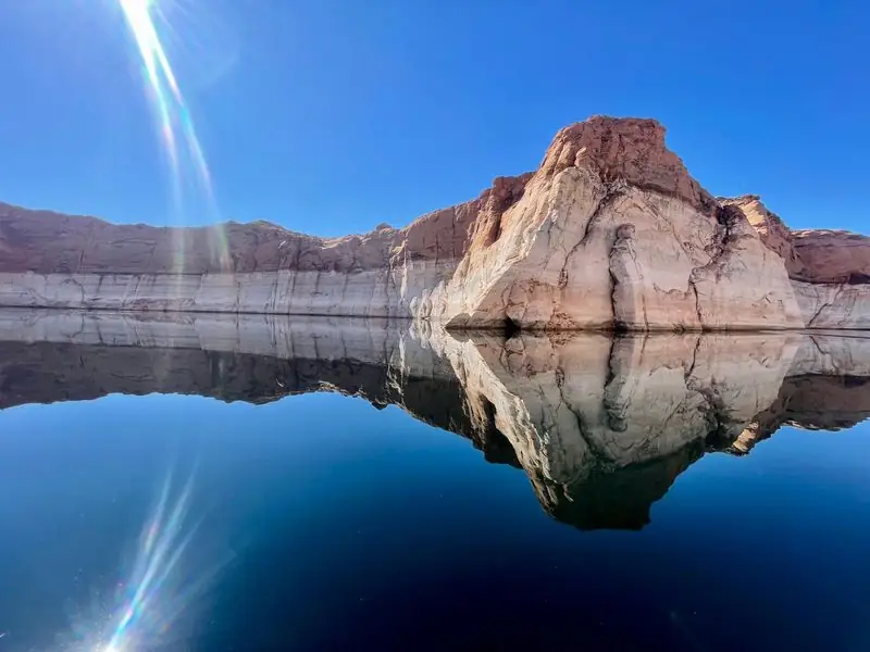 Mirror-calm lake reflecting sandstone cliffs, no people
