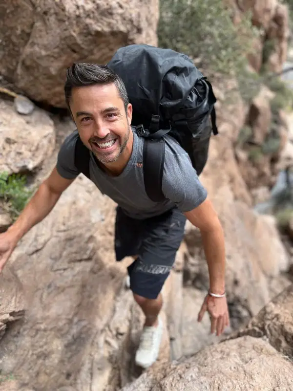 Grinning Travis scrambling canyon rocks with black backpack