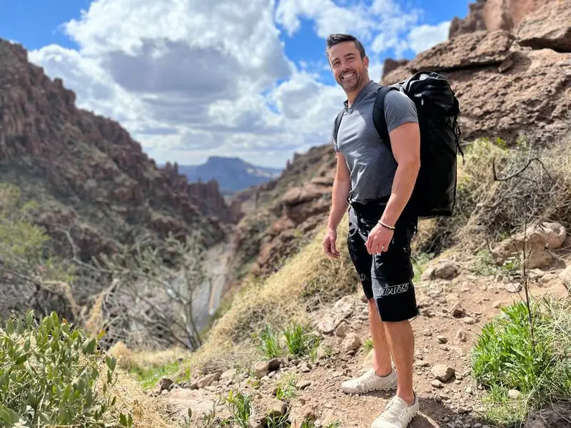 Smiling Travis with black backpack hiking rugged canyon trail