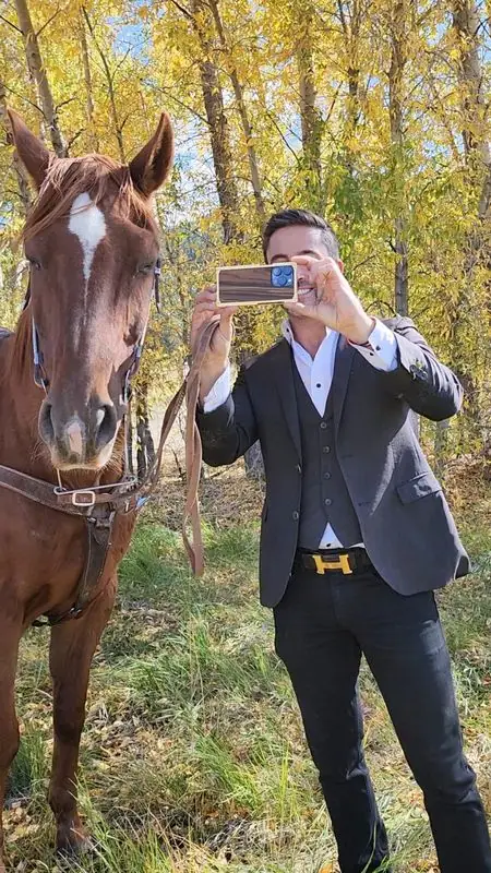 Suited Travis filming chestnut horse among autumn trees