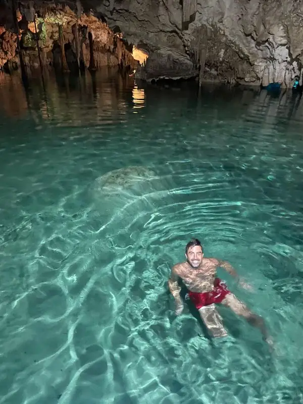 Travis smiling while swimming in turquoise cenote cave