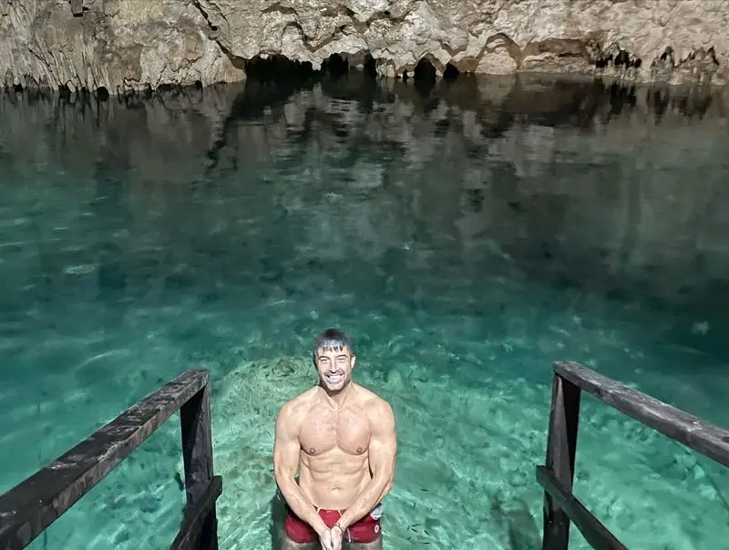 Shirtless Travis standing waist-deep in cave cenote water