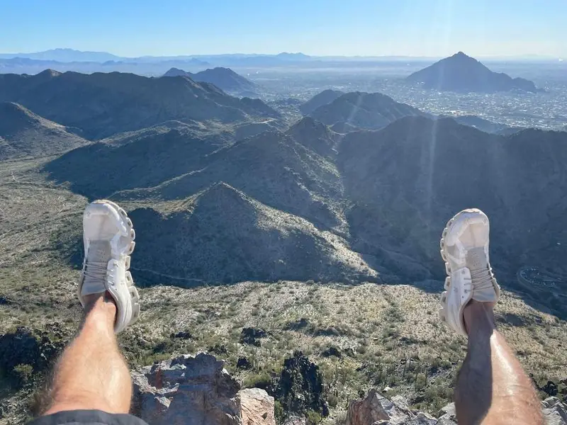 Legs dangling over summit edge, Phoenix valley panorama below