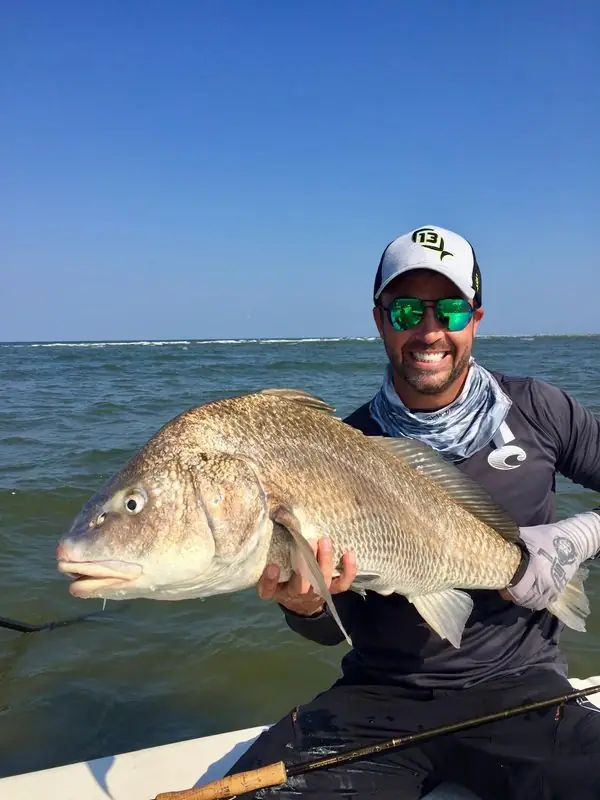 Holding large black drum fish on boat, ocean