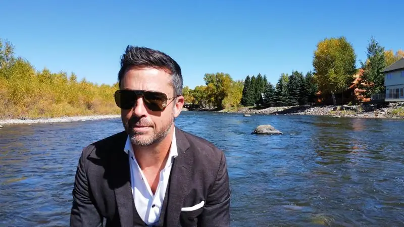 Travis in suit and sunglasses beside autumn river