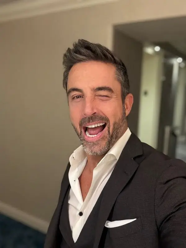 Playful winking selfie in dark suit, hotel hallway
