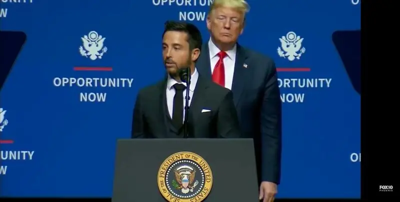Speaking at presidential podium with Trump standing behind