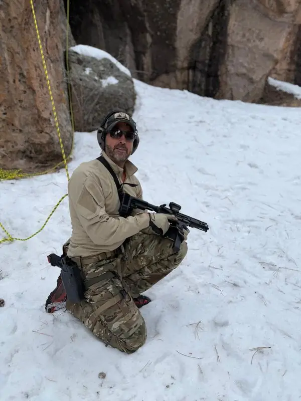 Kneeling in multicam with rifle, snowy crag